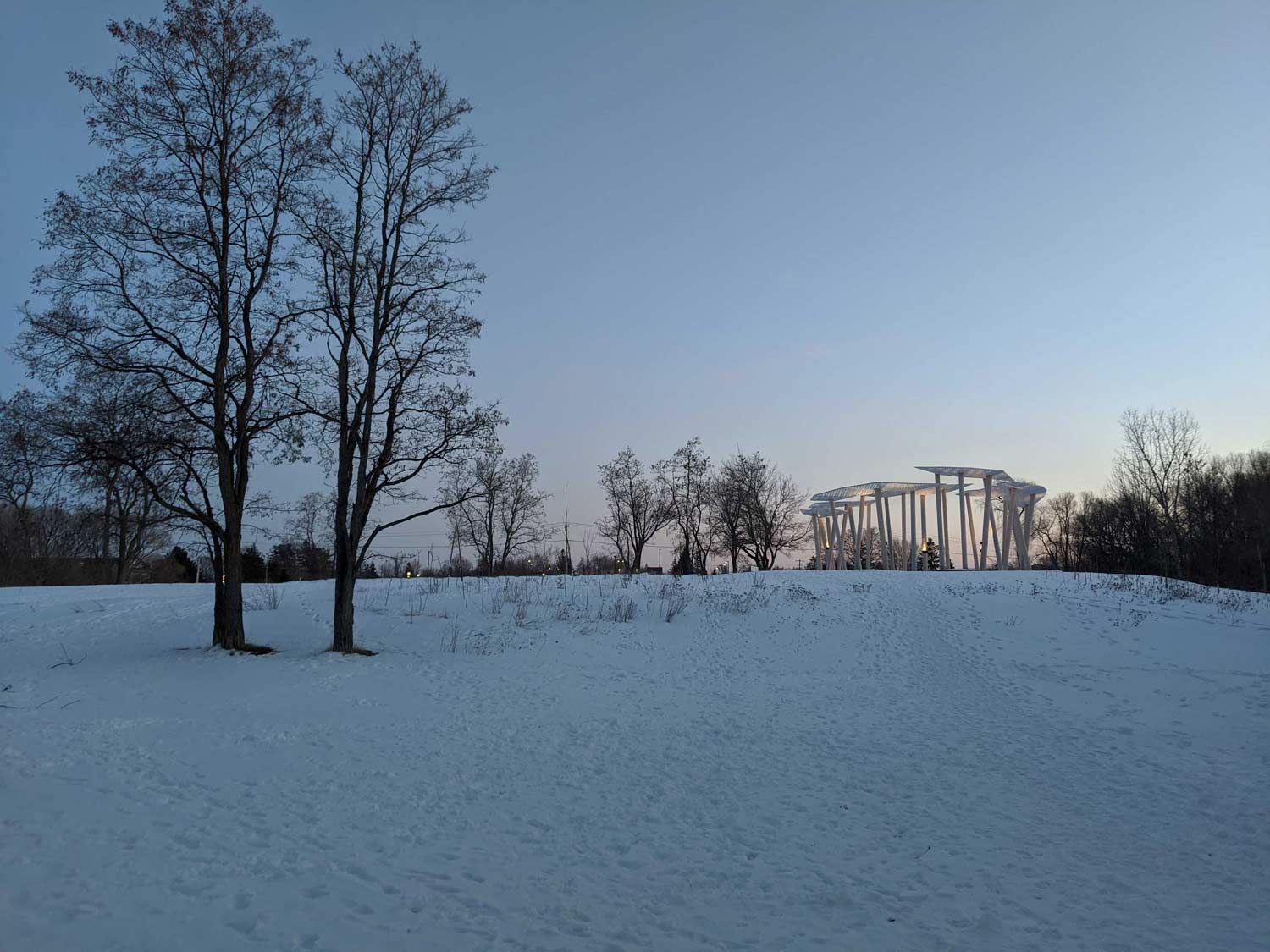 a snow covered field with trees and a building in the background.